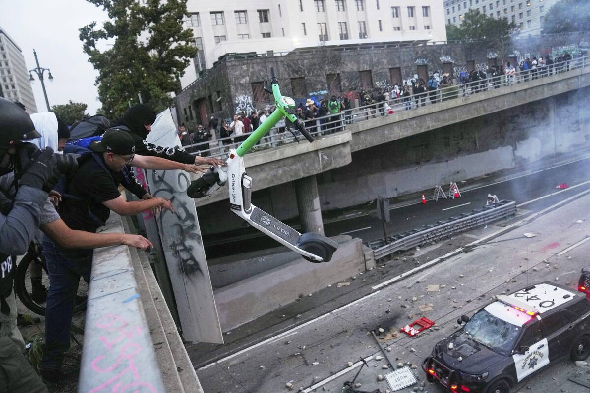 A protester throws a scooter at a police vehical near the metropolitan detention center of down ...