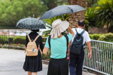 People brave the heat along the Strip by shading themselves with umbrellas on July 31, 2023, in ...