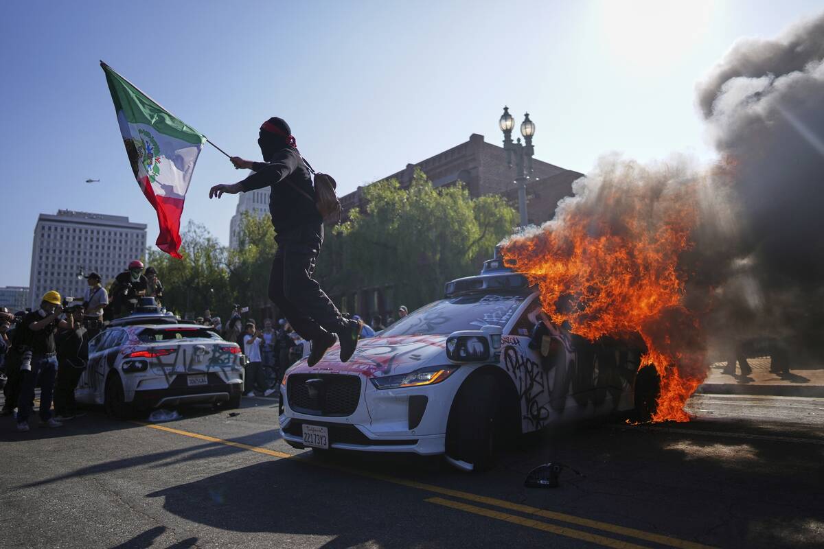 A protester leaps off a burning Waymo taxi near the Metropolitan Detention Center in downtown L ...