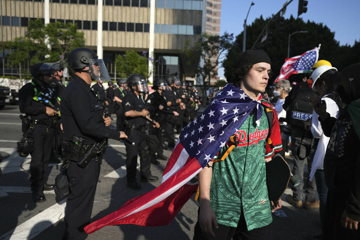 A protester wearing a Los Angeles Dodgers shirt and sporting an American flag as a cape walks p ...