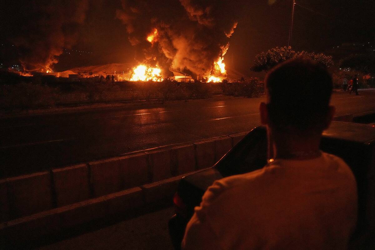 A man looks at flames rising from an oil storage facility after it appeared to have been struck ...