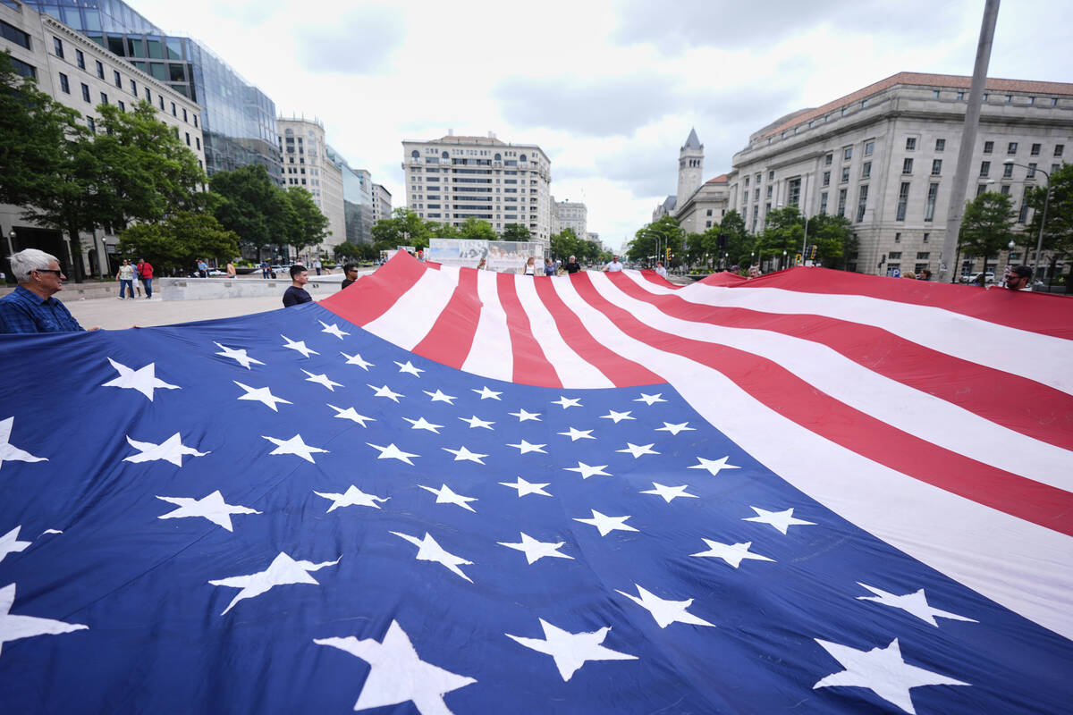 People hold a large American flag at Freedom Plaza before a parade commemorating the Army's 250 ...