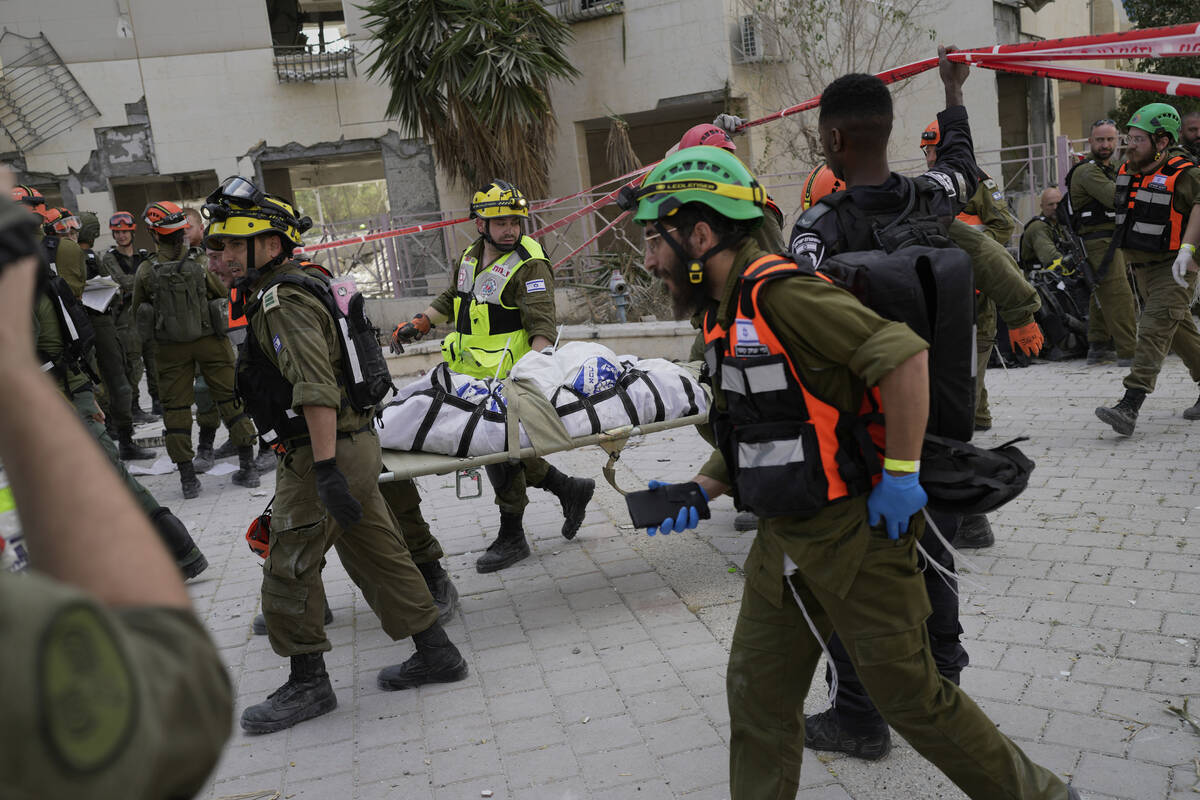 Israeli soldiers and rescue workers carry a body from a residential building destroyed by an Ir ...