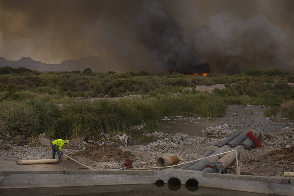 A worker makes adjustments to a water pump as smoke rises from a fire at the Clark County Wetla ...