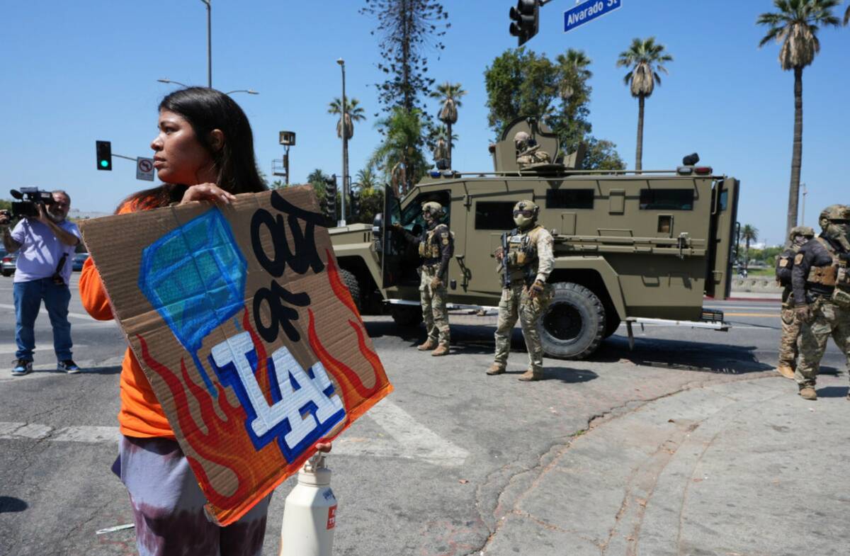 A person holds a sign in front of federal agents at MacArthur Park Monday, July 7, 2025, in Los ...