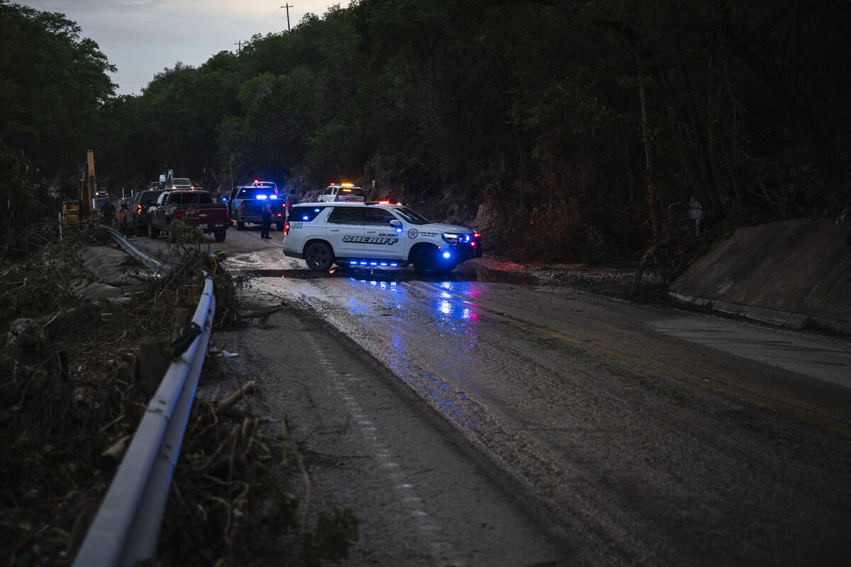 Law enforcement officials block a road along the Guadalupe River as they load an extricated bod ...
