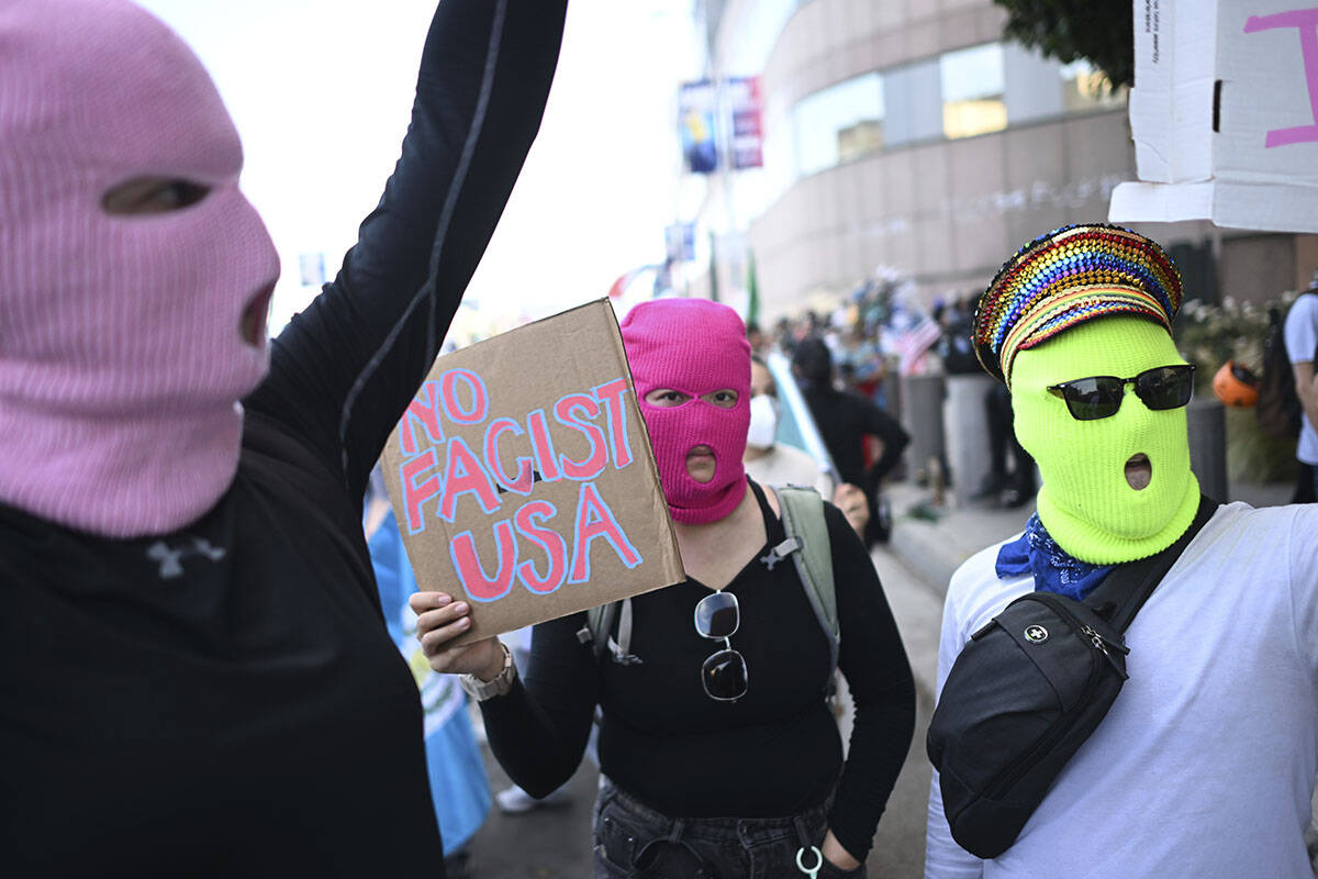 Demonstrators wearing masks hold signs outside the Federal Building during a protest on Friday, ...