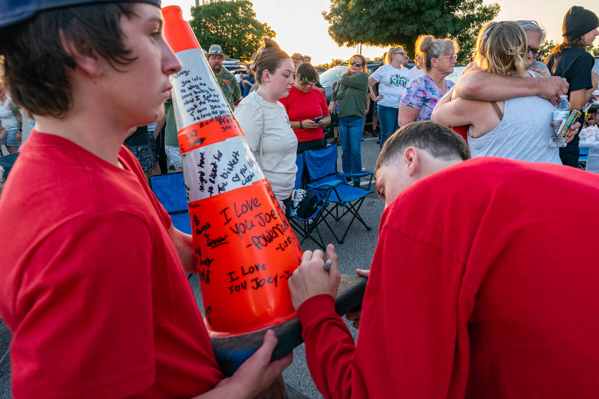 Friends and family write messages on an orange safety cone that was placed by a painted red hea ...