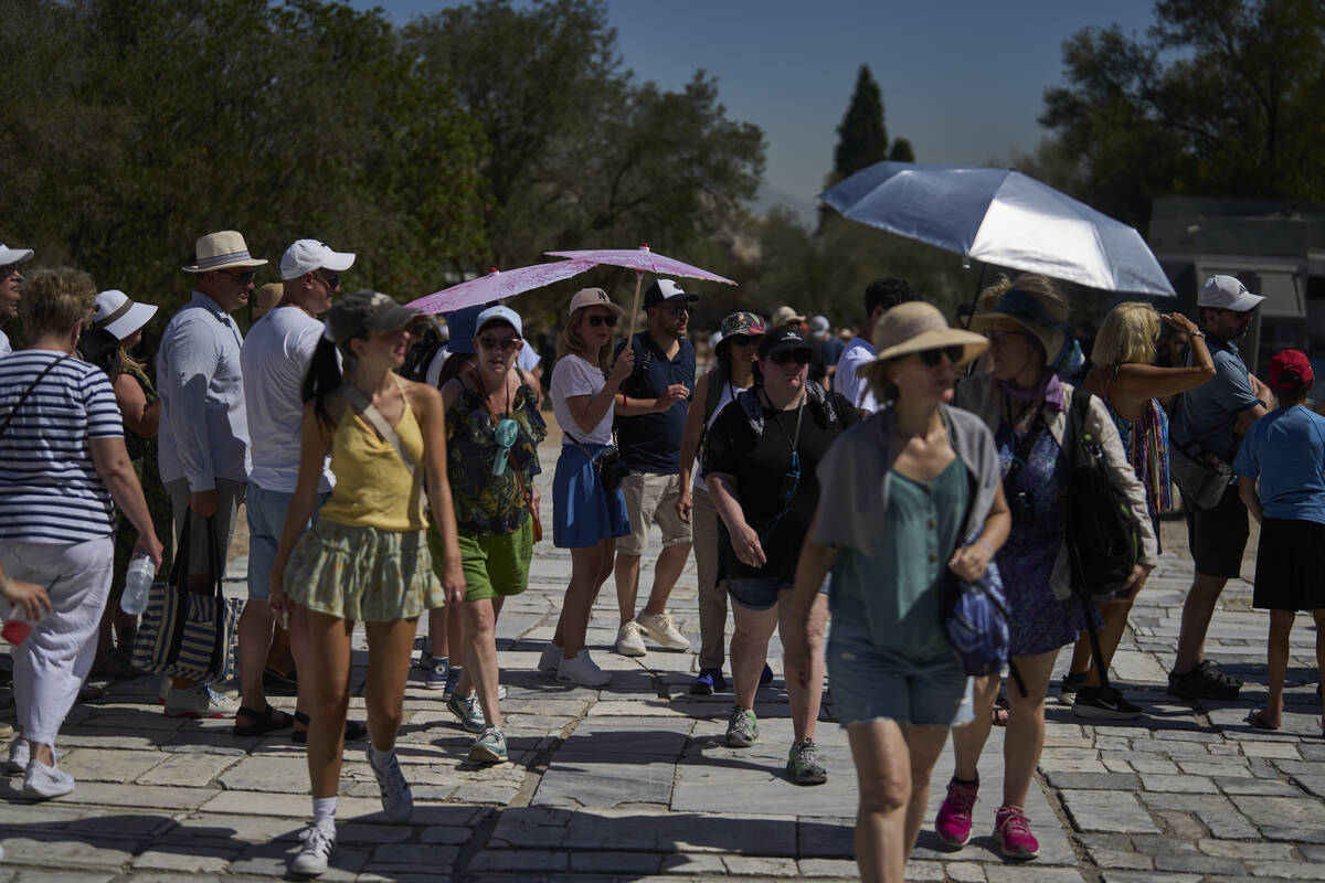 Tourist with umbrellas wait outside the Acropolis of Athens, on Monday , July 7, 2025 while aut ...