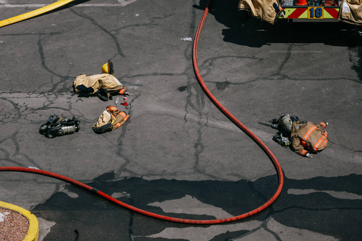 Firefighters’ supplies and water hoses lie on the parking lot as they work to douse the still ...