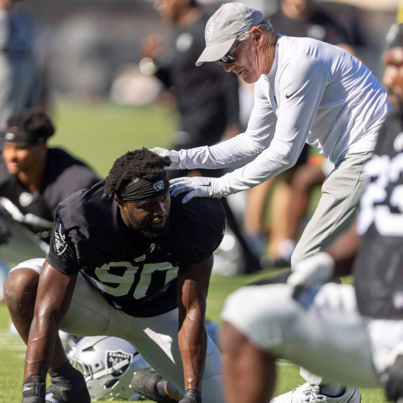 Raiders head coach Pete Carroll playffully pushes Raiders defensive end Ovie Oghoufo (90) durin ...