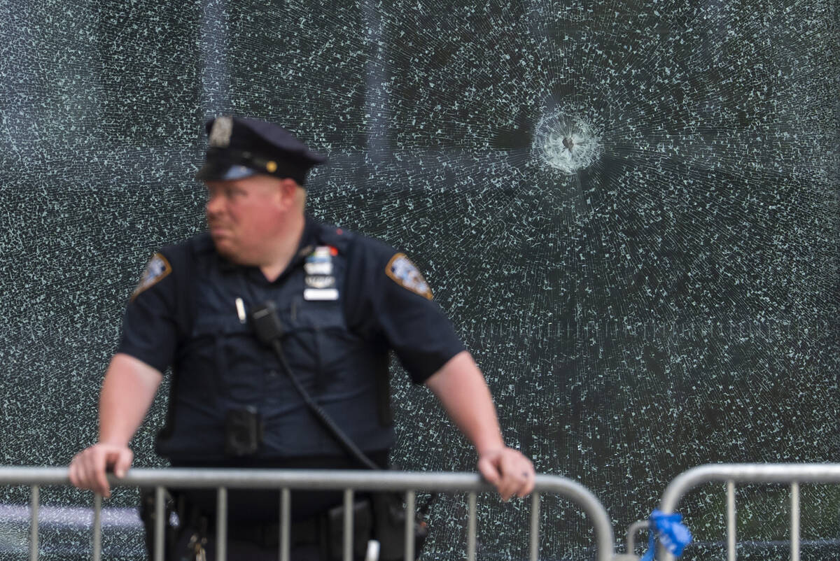 An NYPD officer stands in front of glass shattered from a bullet hole at the scene of Monday's ...