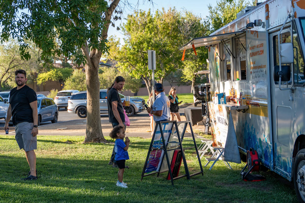 Customers wait for their orders in front of food trucks parked at the Bruce Trent Park Farmers ...