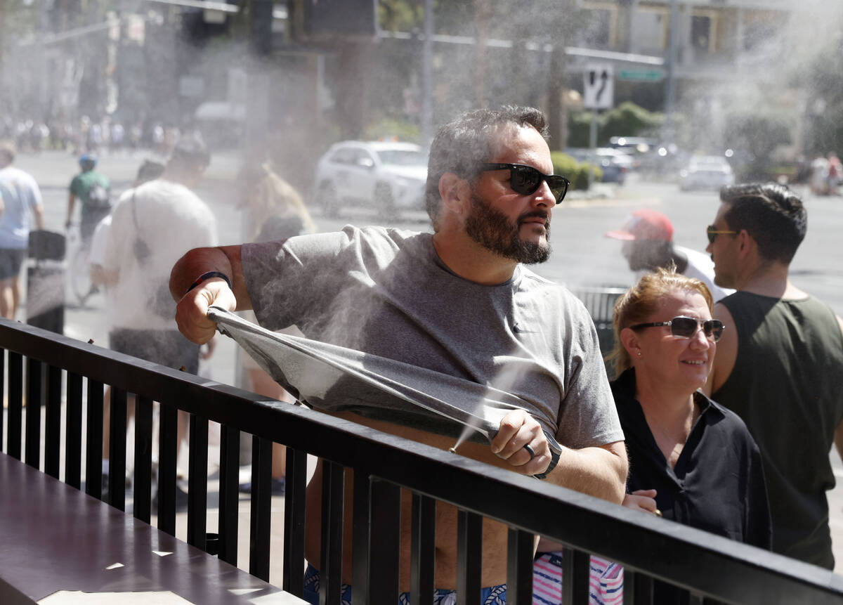 As the temperature climbs towards triple digits, a pedestrian cools off with water misters alon ...
