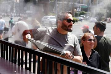 As the temperature climbs towards triple digits, a pedestrian cools off with water misters alon ...