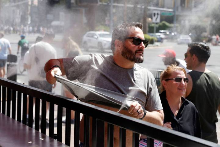 As the temperature climbs towards triple digits, a pedestrian cools off with water misters alon ...