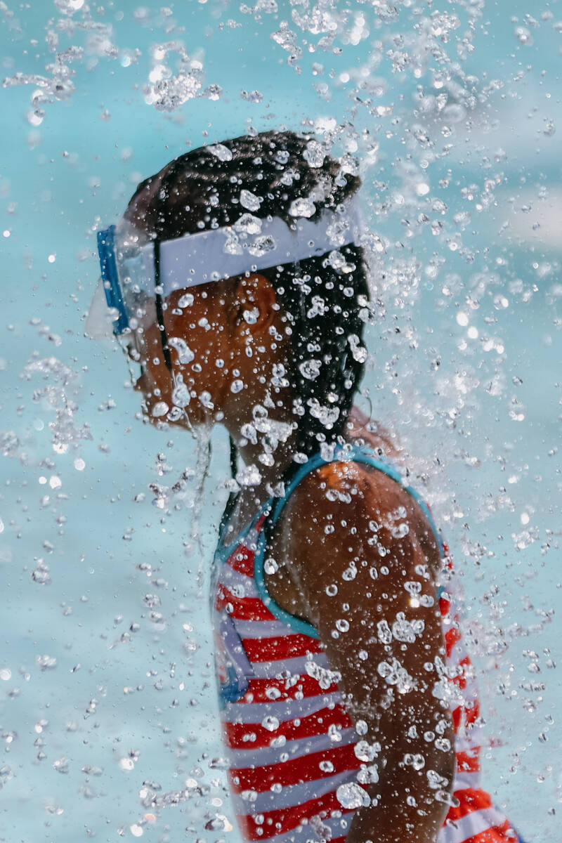 A child wearing a scuba mask runs in and out of the falling water in the shallow end of the poo ...