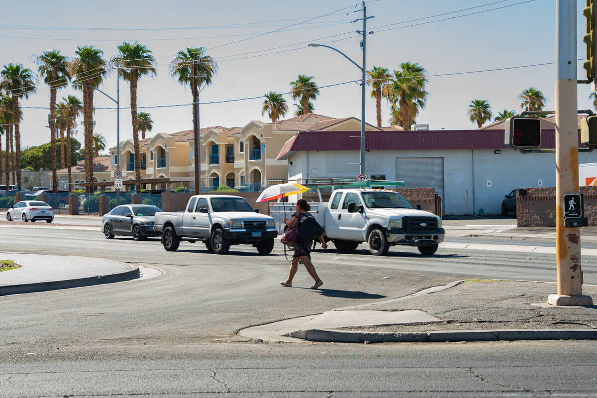 A woman uses an umbrella to shield herself from the sun while crossing the street on a hot afte ...