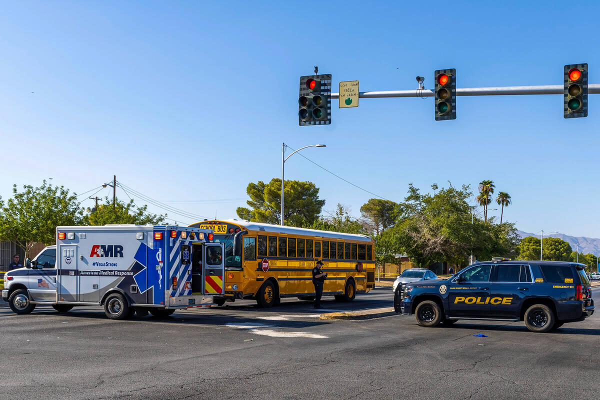 Clark County School District officers stand beside a damaged school bus while emergency crews e ...