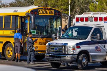 A Clark County School District officer signals others beside a damaged school bus while emergen ...