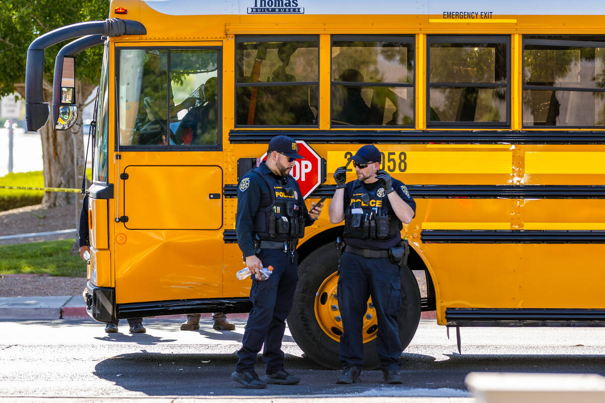 Clark County School District officers stand beside a damaged school bus while emergency crews e ...