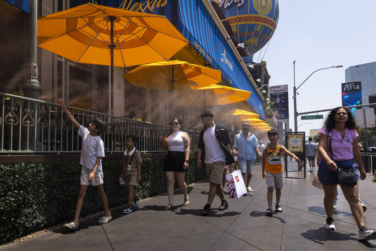 People cool off by misters while walking along the Las Vegas Strip near Paris Las Vegas as temp ...