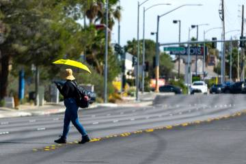 A pedestrian stays cool beneath a yellow umbrella while crossing Eastern Avenue on May 29, 2025 ...
