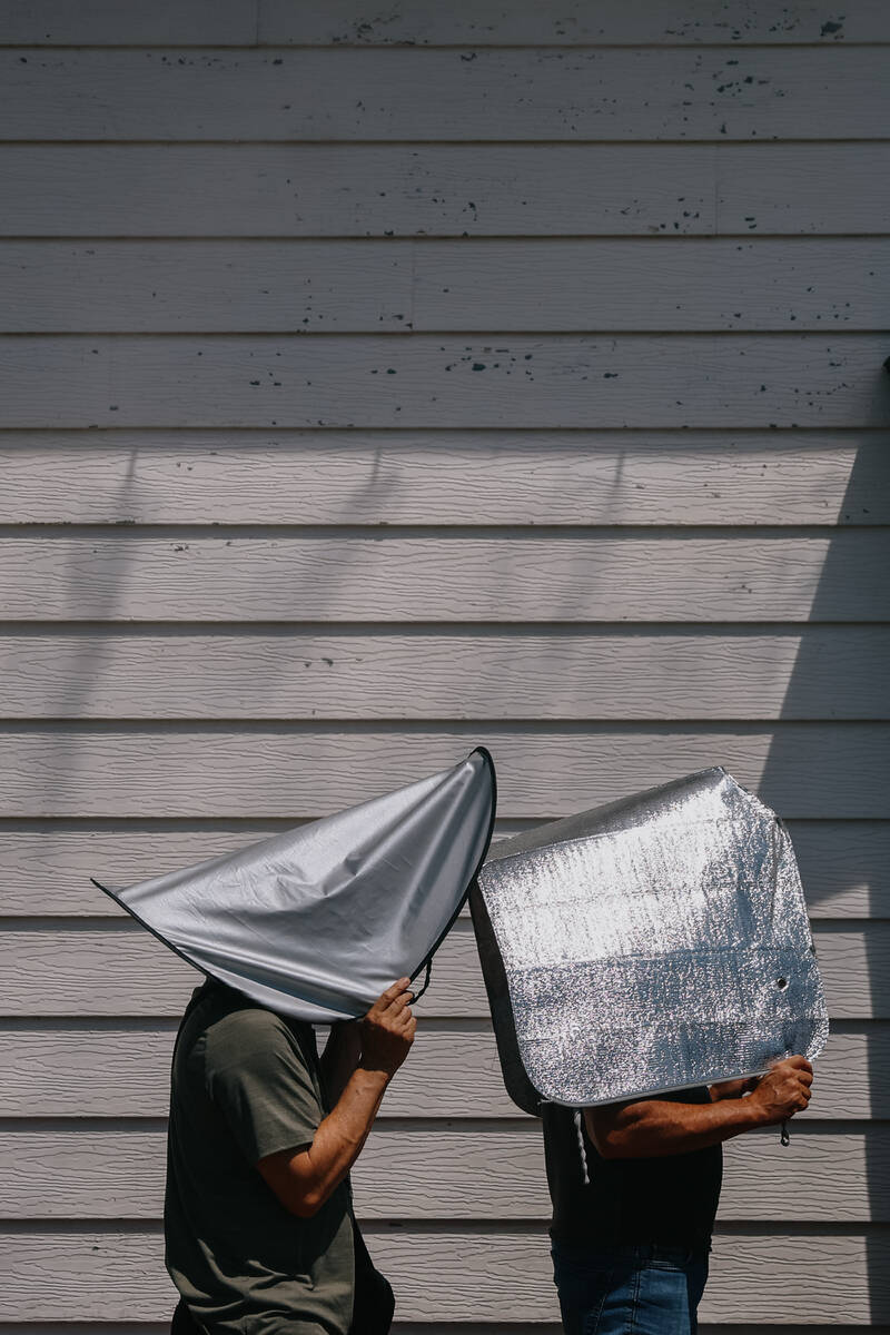 Two people use windshield sun shades to take cover from the sun as they wait in line to purchas ...