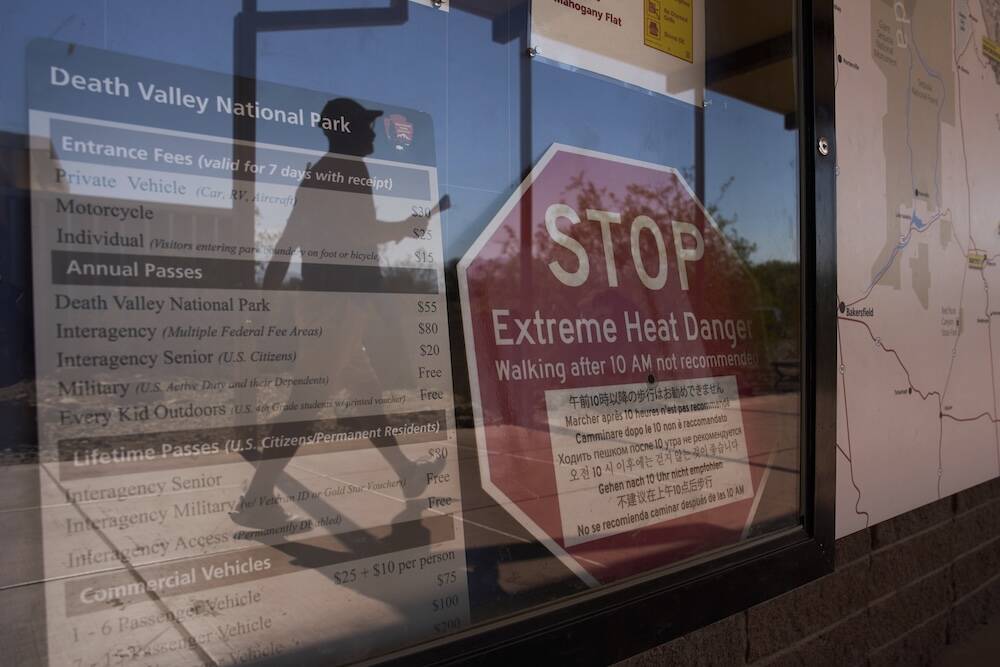 A person walks by a sign warning of extreme heat danger at the Furnace Creek Visitor Center, Su ...