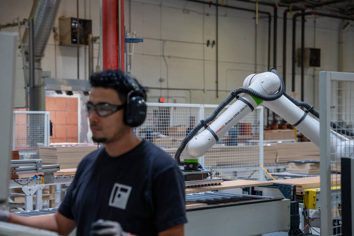 A worker stands in front of a cooperative robot on the factory floor at the Foliot Furniture ma ...