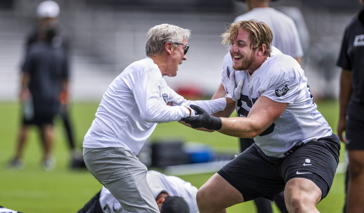 Raiders head coach Pete Carroll grapples with Raiders guard Alex Cappa (65) while stretching du ...