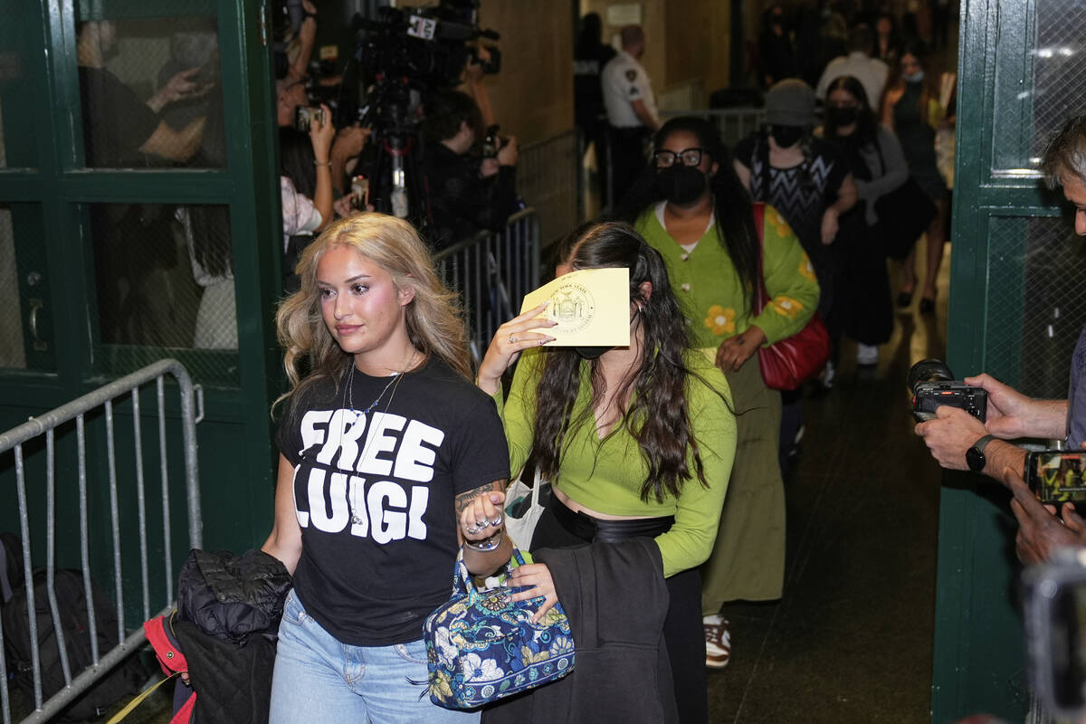 Members of the public, including a woman wearing a "Free Luigi" shirt, enter a courtr ...
