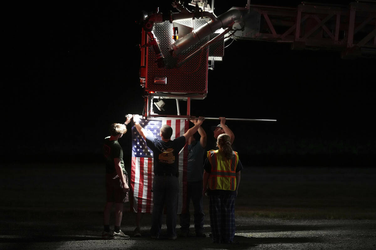 Firefighters attach an American flag to a firetruck before a procession after multiple police o ...