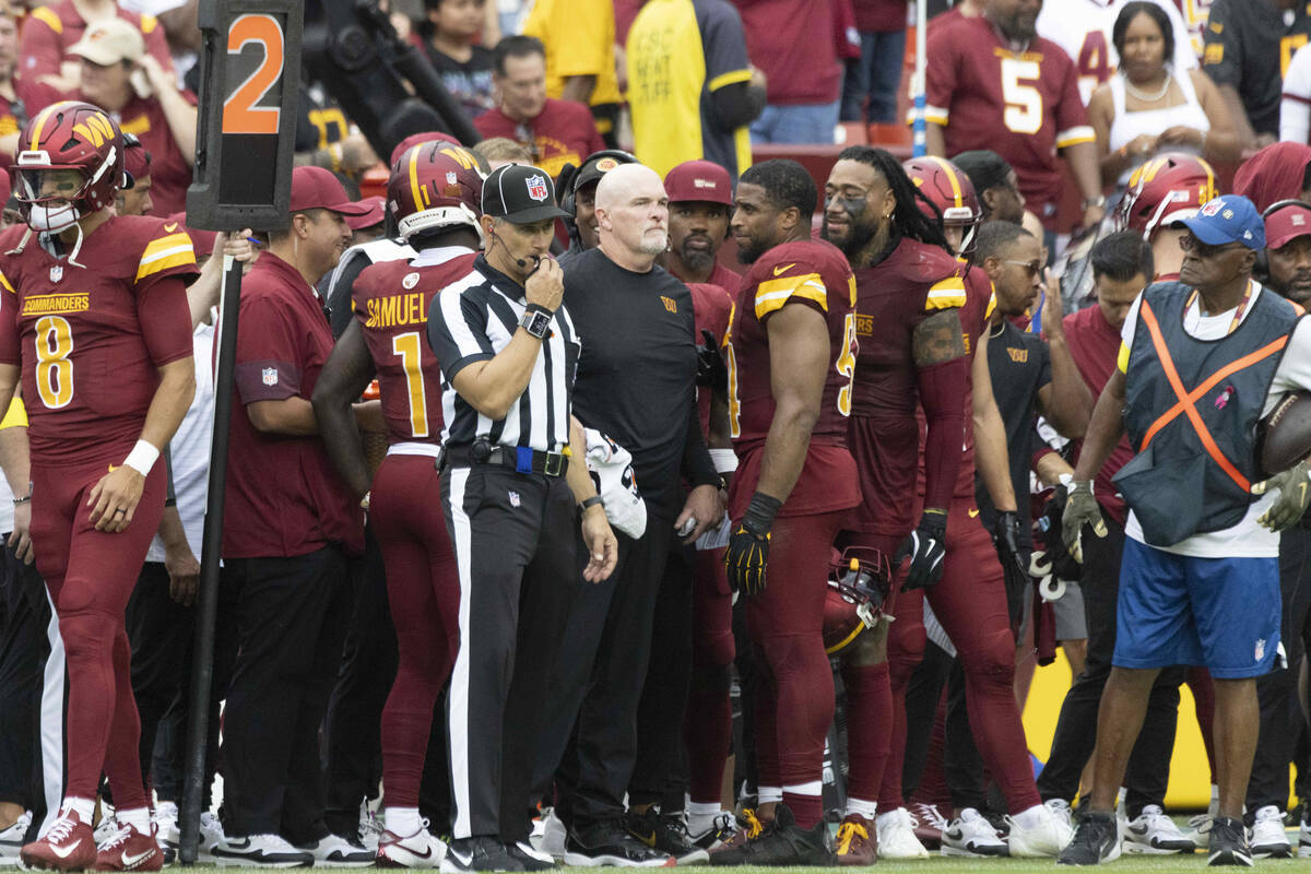 Washington Commanders head coach Dan Quinn, center, is checked on by Washington Commanders midd ...