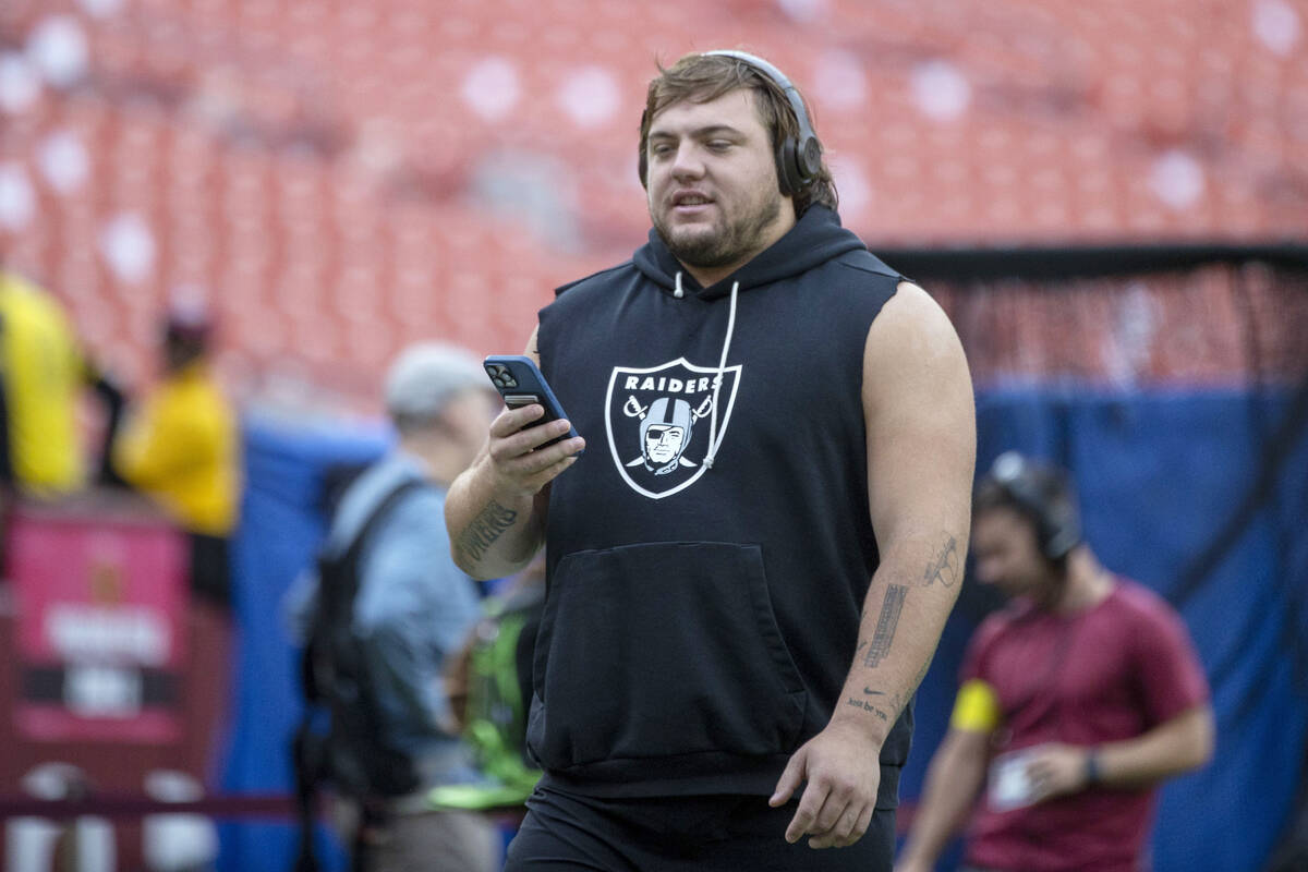 Raiders guard Jackson Powers-Johnson takes a phone call while he warms up on the field before a ...