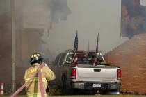 A vehicle that was rammed into the building is surrounded by smoke as a firefighter works on th ...