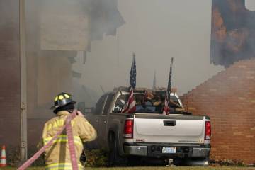 A vehicle that was rammed into the building is surrounded by smoke as a firefighter works on th ...
