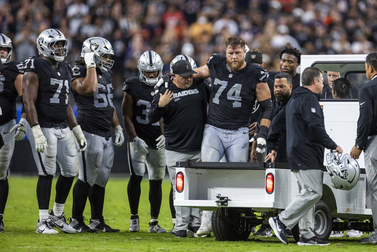 Raiders offensive tackle Kolton Miller (74) is assisted off the field as teammates gather aroun ...