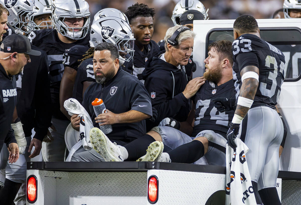 Raiders head coach Pete Carroll consolesa offensive tackle Kolton Miller (74) as he is assisted ...