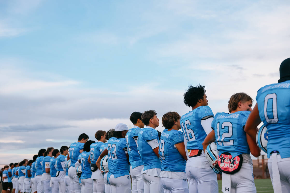 The team lines up along the sidelines for the playing of the national anthem before a football ...