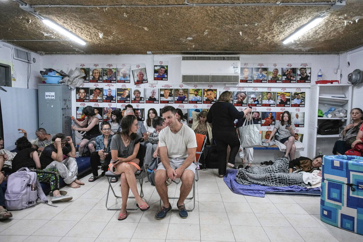 People sit next to photographs of Israeli hostages abducted by Hamas in Gaza as they take shelt ...
