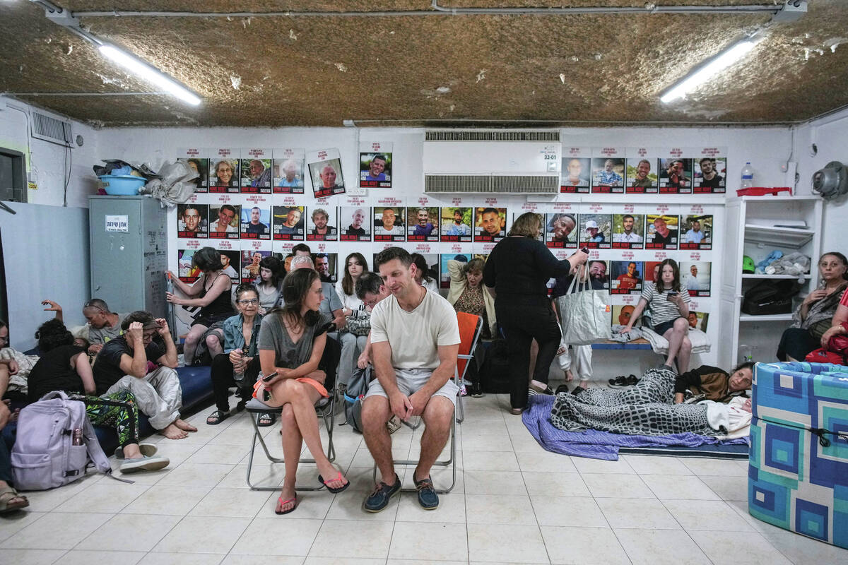 People sit next to photographs of Israeli hostages abducted by Hamas in Gaza as they take shelt ...