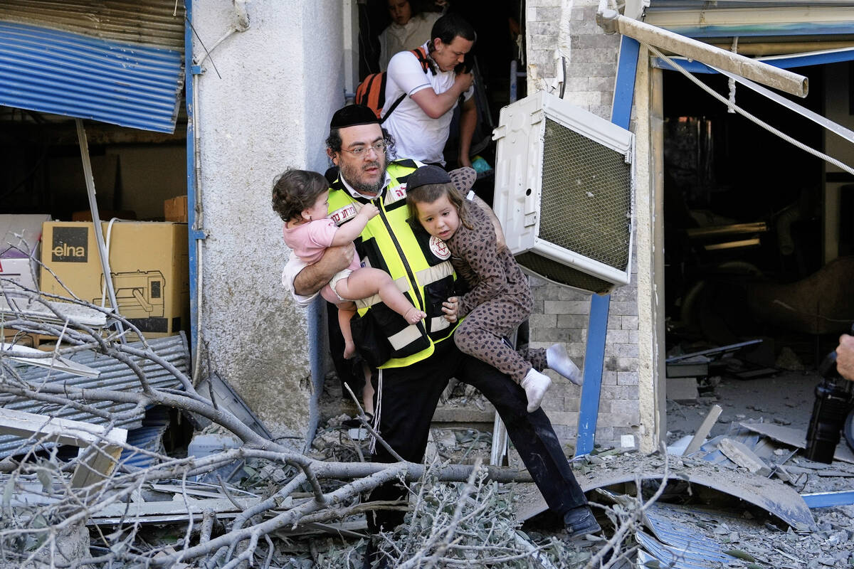 A rescue worker evacuates two children from the site where a missile launched from Iran struck ...