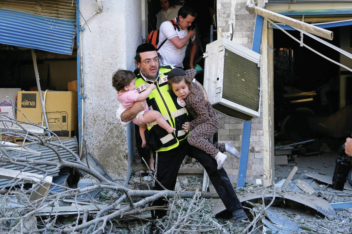 A rescue worker evacuates two children from the site where a missile launched from Iran struck ...