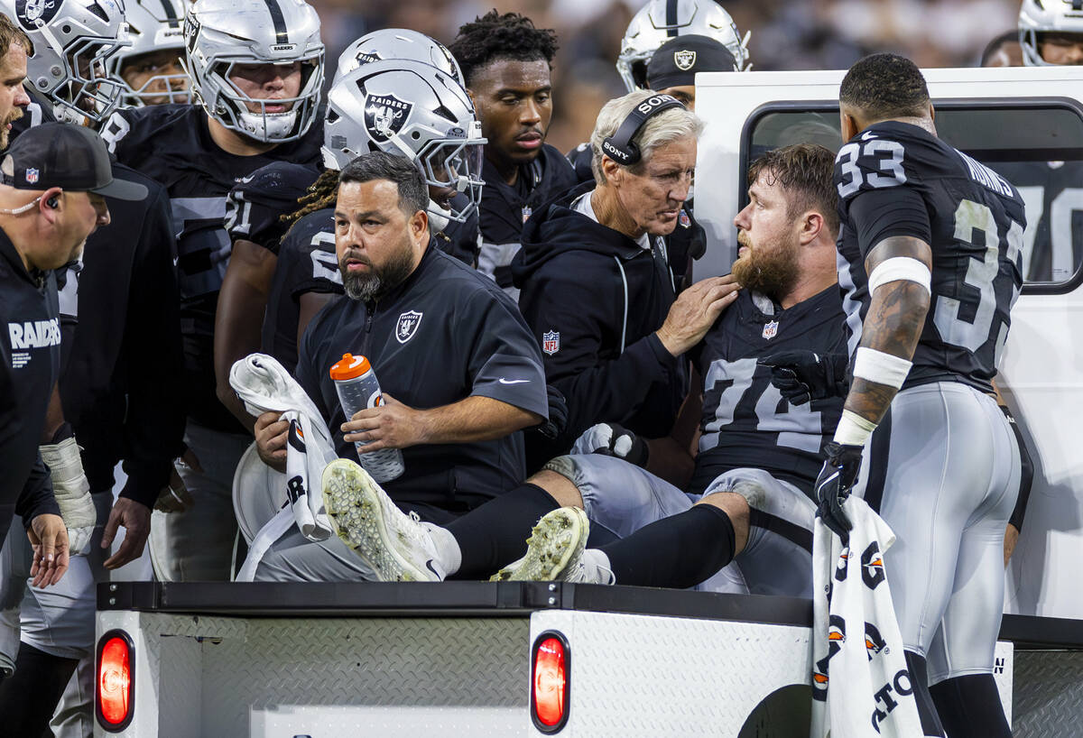 Raiders head coach Pete Carroll consoles offensive tackle Kolton Miller (74) as he is assisted ...
