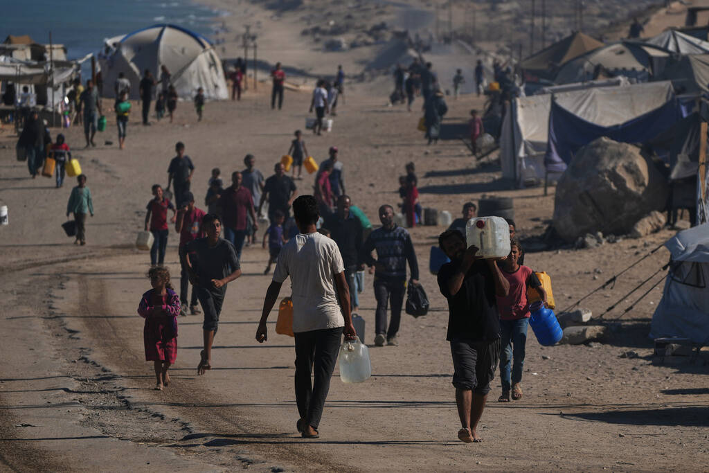 Palestinians carry plastic bottles with water in an area of a makeshift tent camp for displaced ...