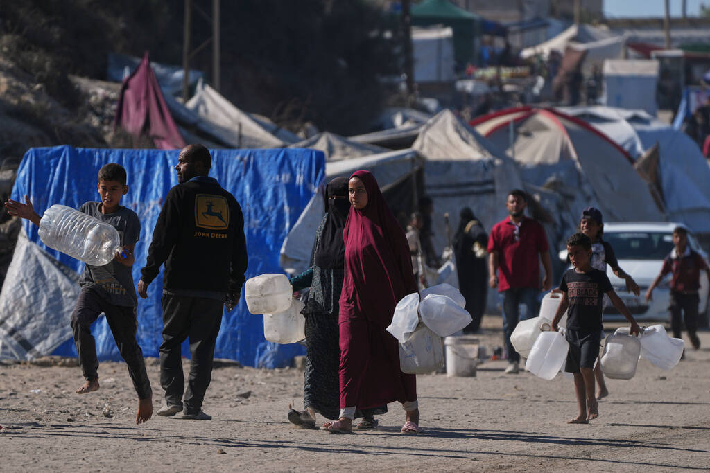 Palestinians carry plastic bottles to collect water in an area of a makeshift tent camp for dis ...
