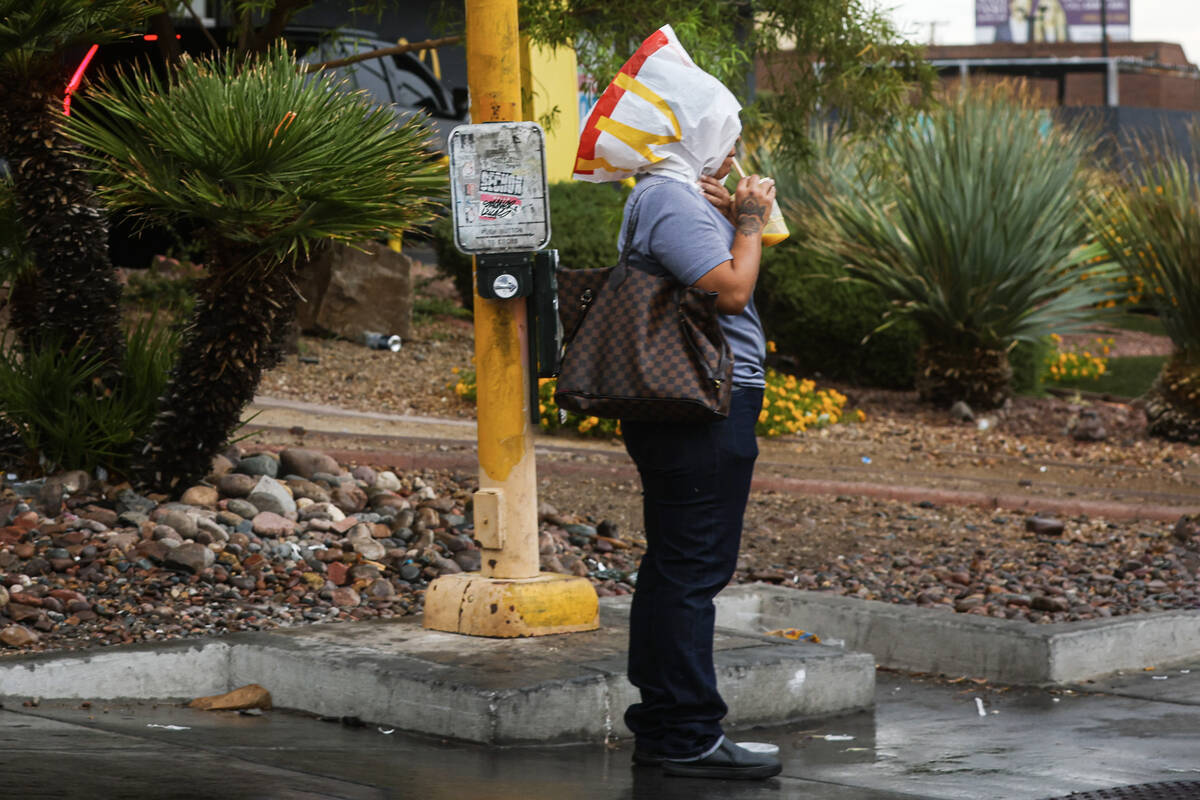 A woman uses a McDonald’s bag to stay covered from the rain while waiting at a crosswalk ...