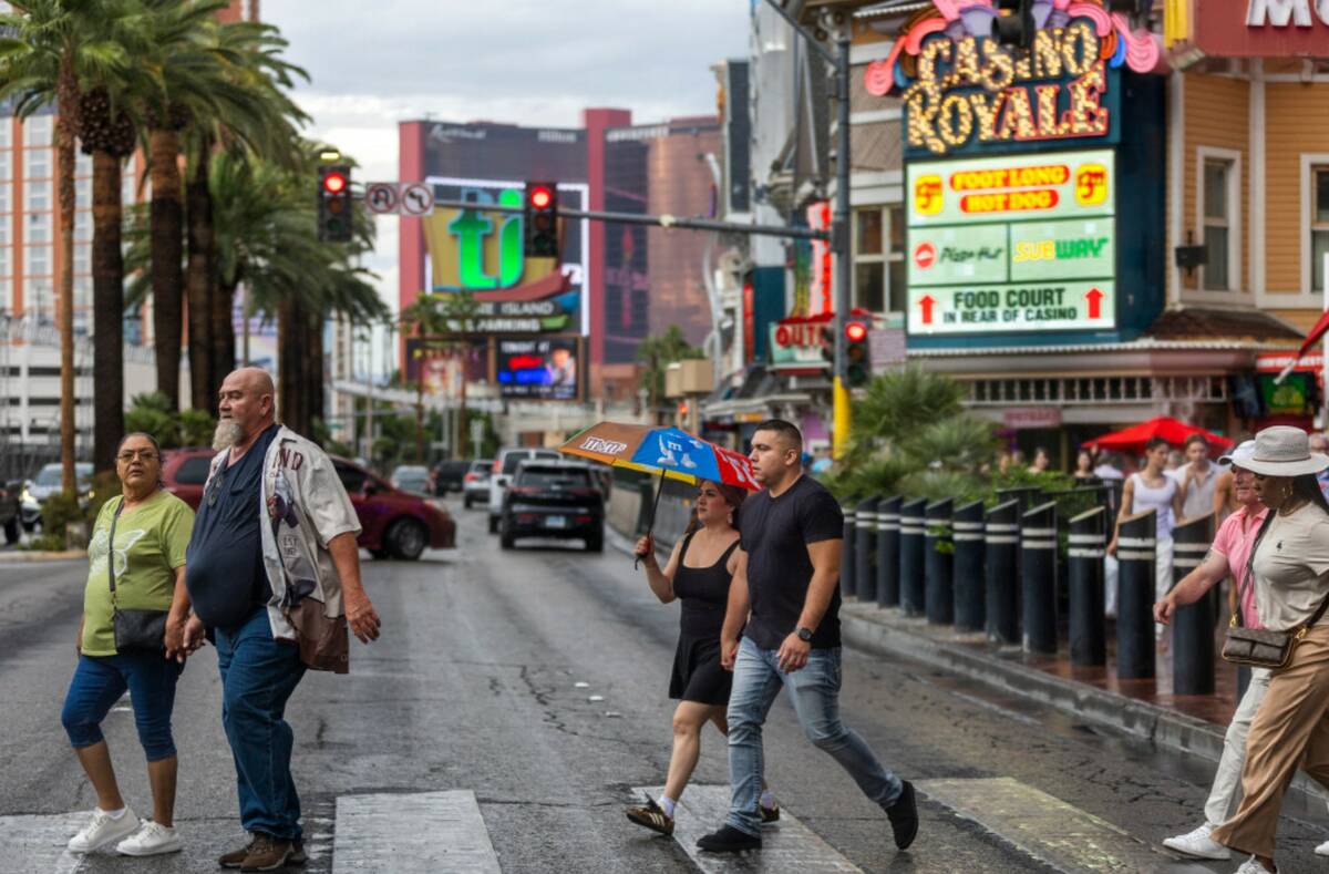 A pedestrian uses an umbrella amongst others while crossing Las Vegas Boulevard as rain moves t ...