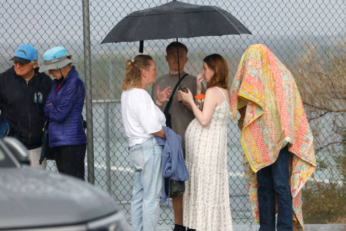 Fans hold umbrellas to protect themselves from heavy rain as they line up to attend a high scho ...